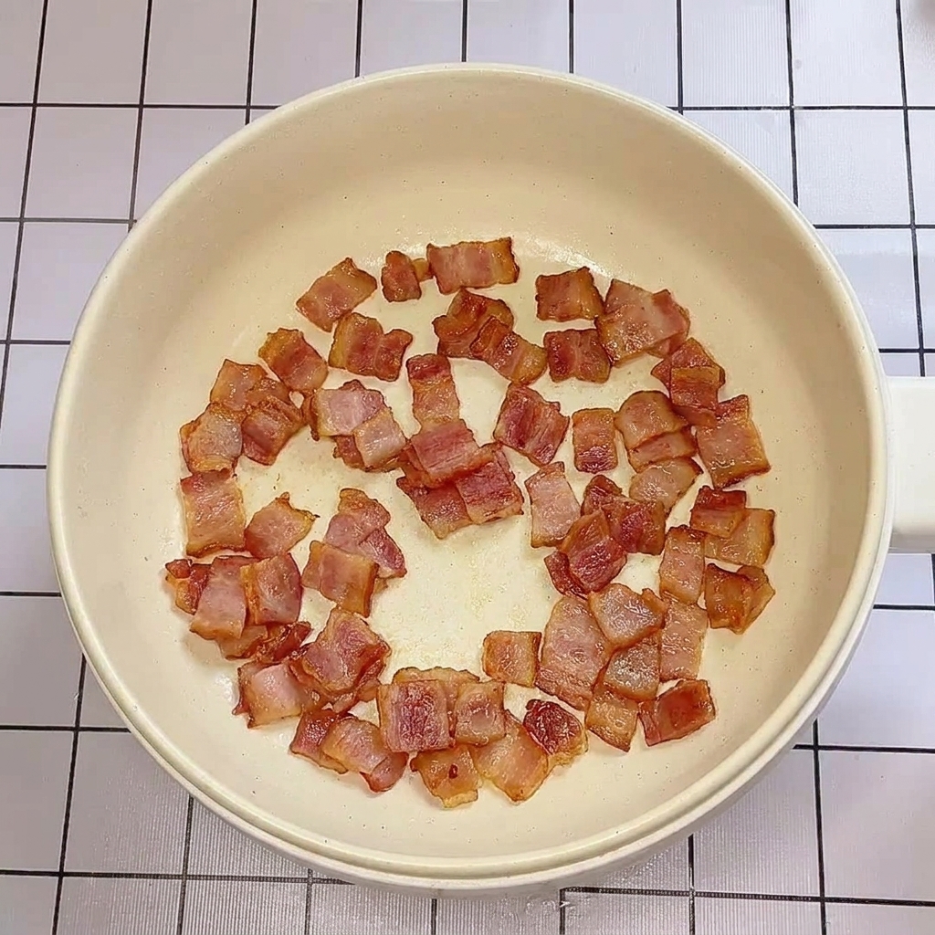Des morceaux de lardons dorés et croustillants cuisant dans une poêle.