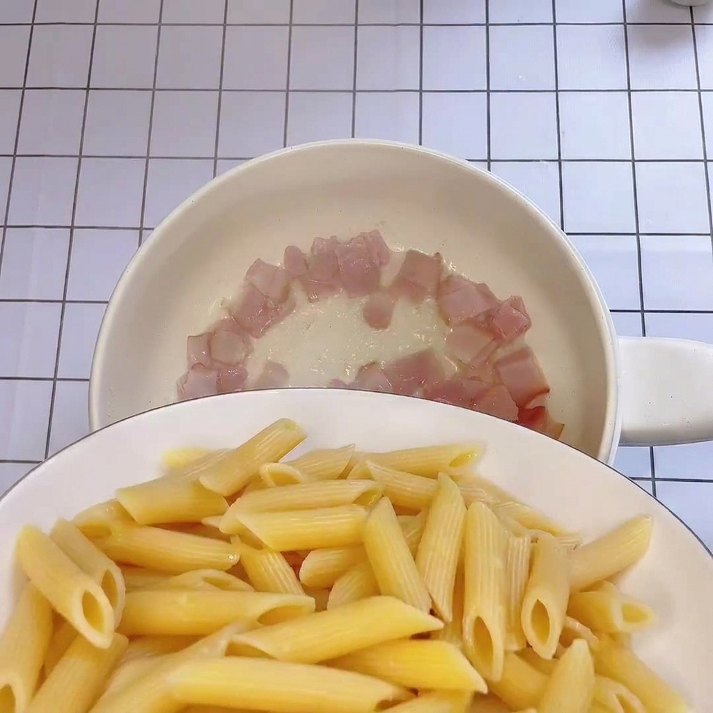 Les pennes fraîchement cuites ajoutées dans la poêle contenant les lardons croustillants.