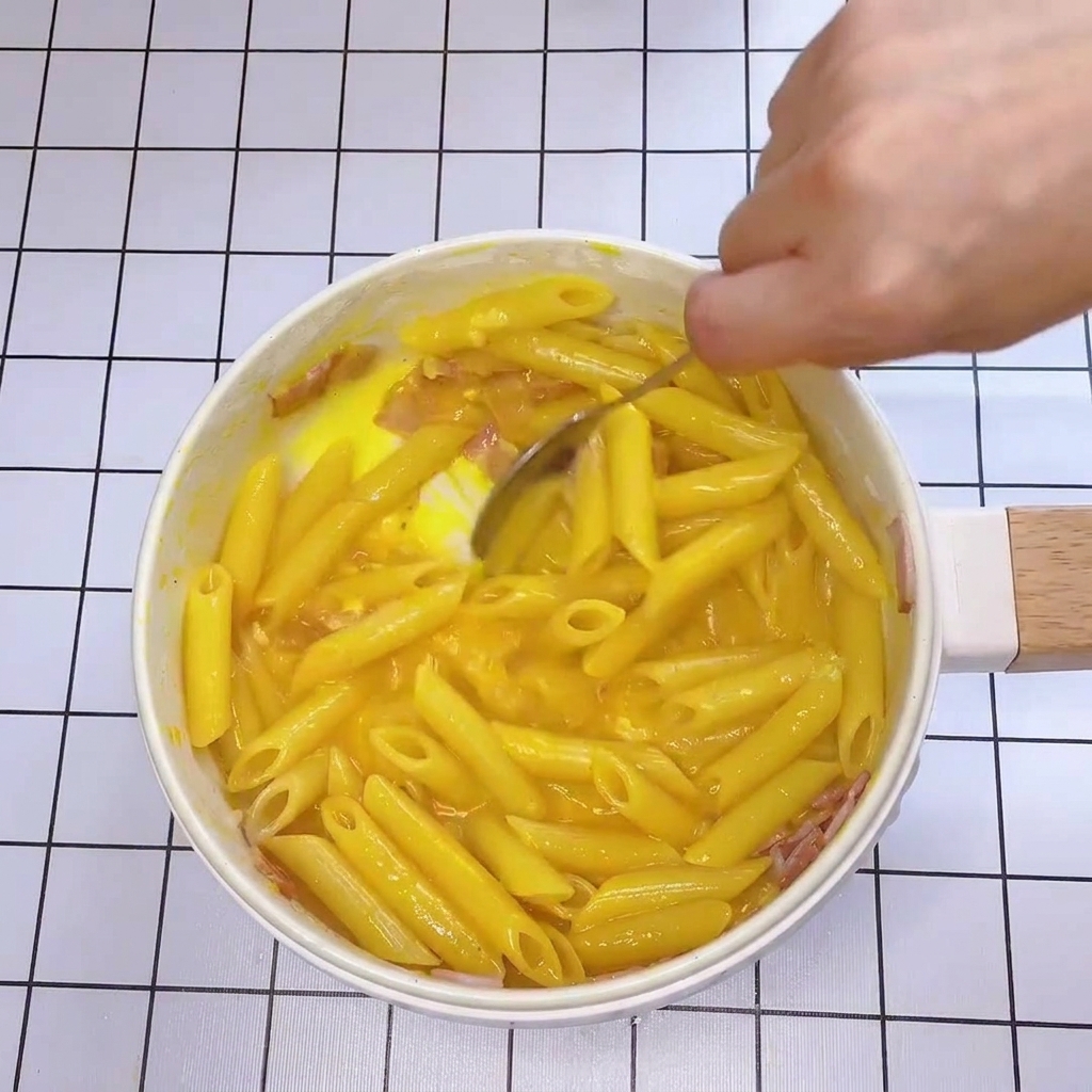 Gros plan dune cuillère mélangeant rapidement les pâtes et les lardons avec une sauce épaisse et crémeuse.