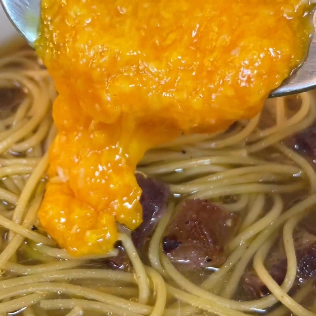 Un mélange dœufs et de fromage riche et orangé versé sur les pâtes dans la poêle.