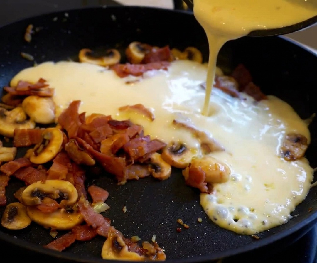 Des pâtes cuites ajoutées dans la poêle remplie de sauce crémeuse aux lardons et champignons.