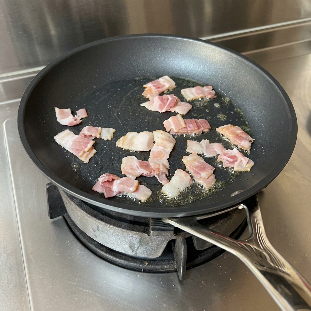 Lanières de bacon cuisant dans une poêle avec de lhuile, remuées par une spatule rouge.