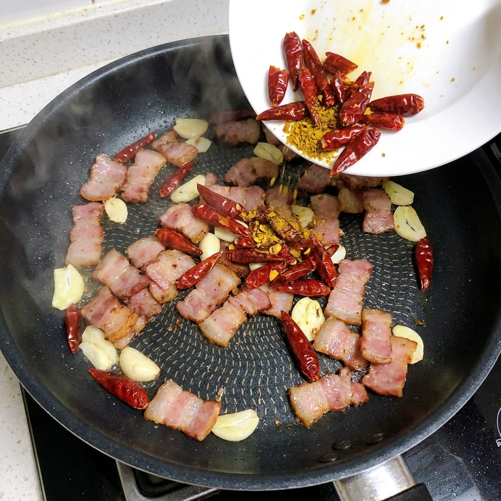 Tranches dail et piments rouges séchés ajoutés dans une poêle contenant des lanières de bacon en cours de cuisson.