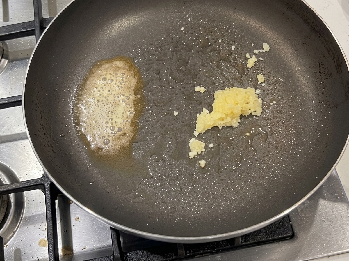 Pâtes mélangées, enrobées dail, de morceaux de lard et de piment dans une grande poêle.
