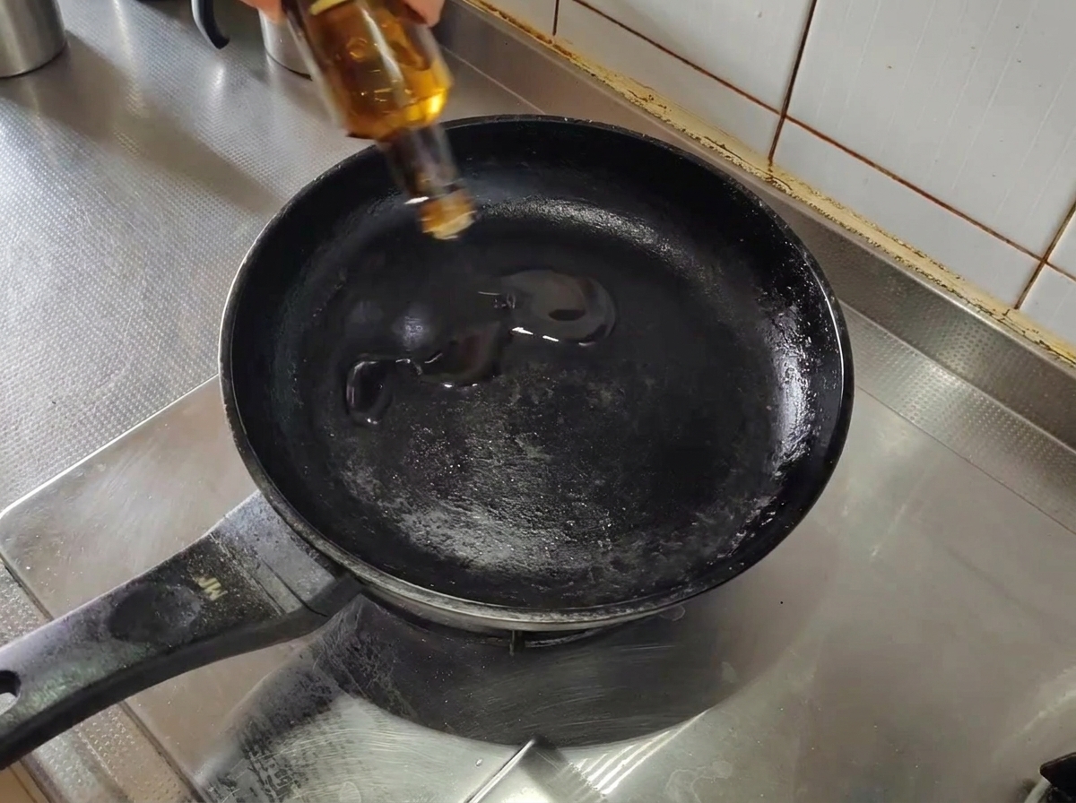 Huile dolive versée dans une poêle noire vide préchauffée sur une cuisinière.
