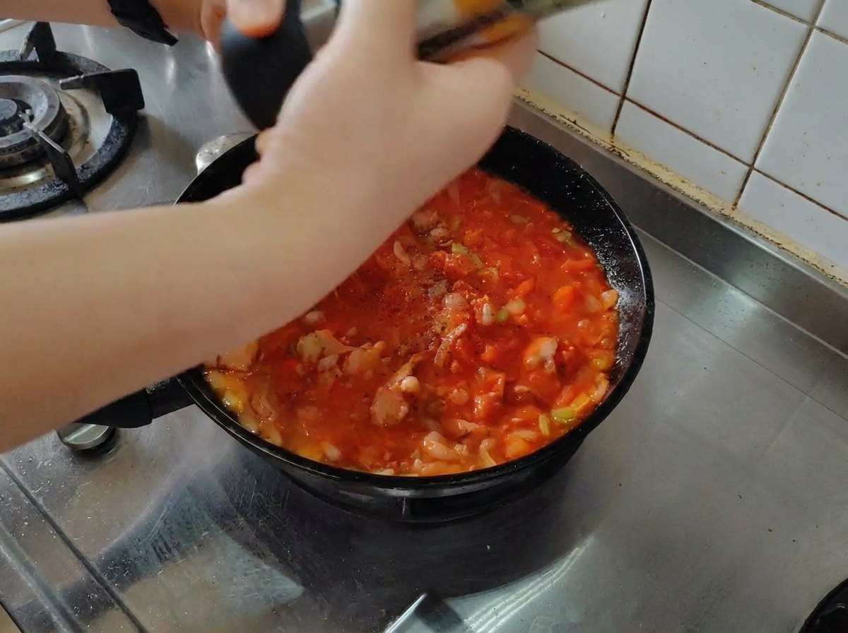 Poivre noir fraîchement moulu au-dessus dune sauce tomate et lard mijotant dans une poêle.