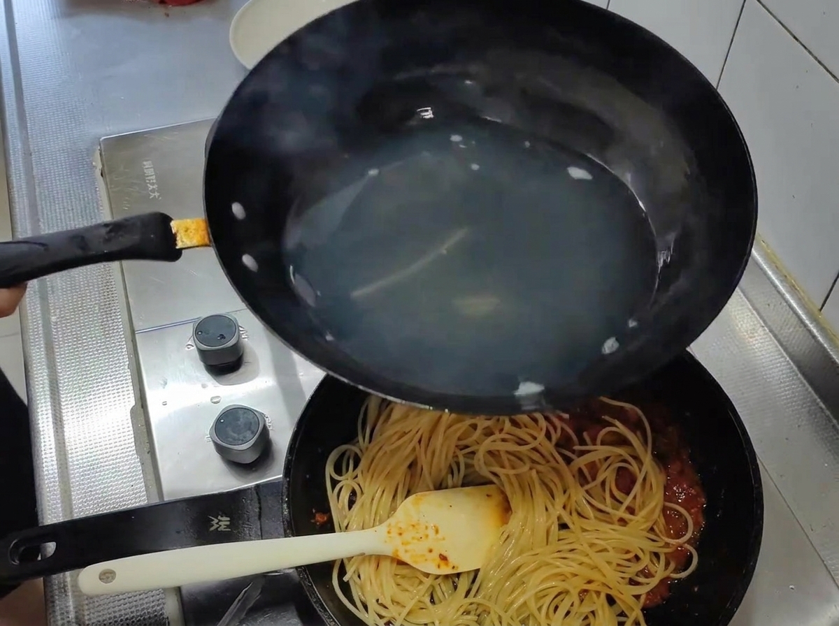 Spaghetti cuits transférés de leau bouillante dans une poêle contenant une riche sauce tomate rouge.