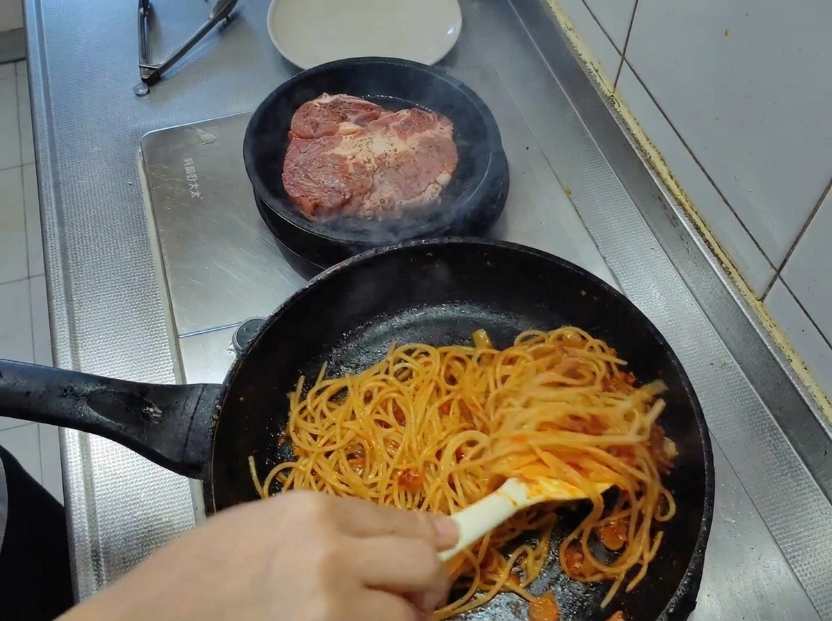 Spaghetti mélangés avec des pinces dans une poêle, devenant entièrement enrobés dune sauce tomate épaisse et vibrante.