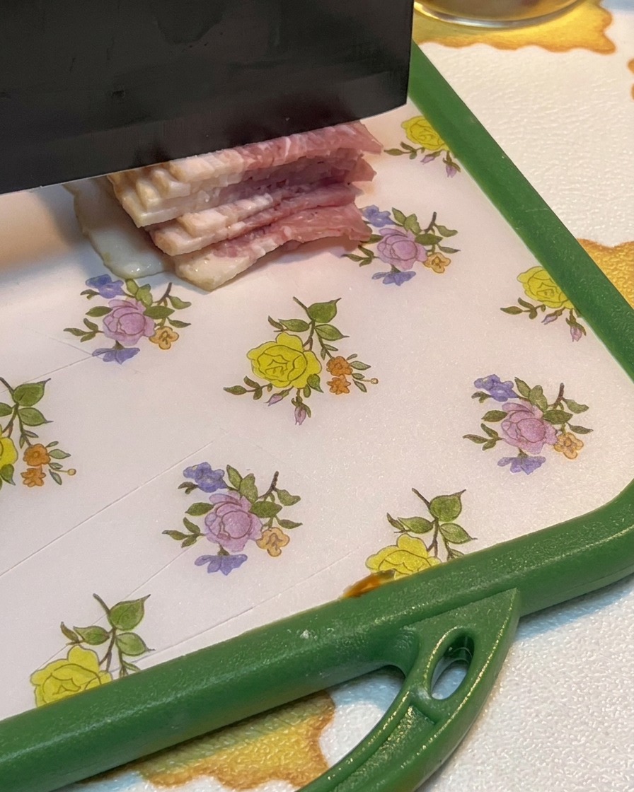 Tranches de bacon cru coupées en petits morceaux sur une planche à découper.