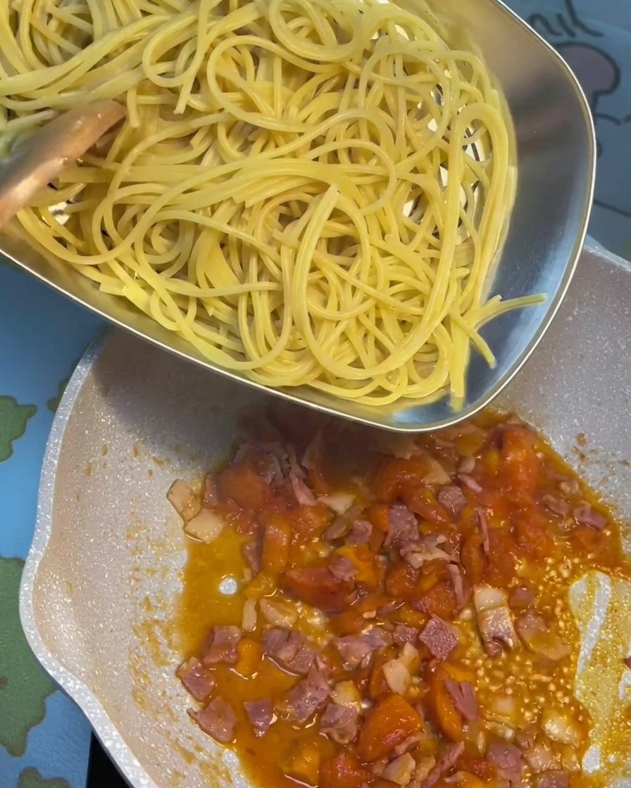 Pâtes cuites incorporées dans la poêle contenant la sauce tomate au bacon.