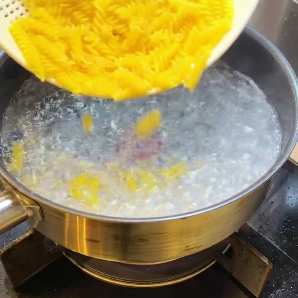 Des pâtes fusilli crues versées dans une casserole deau bouillante.