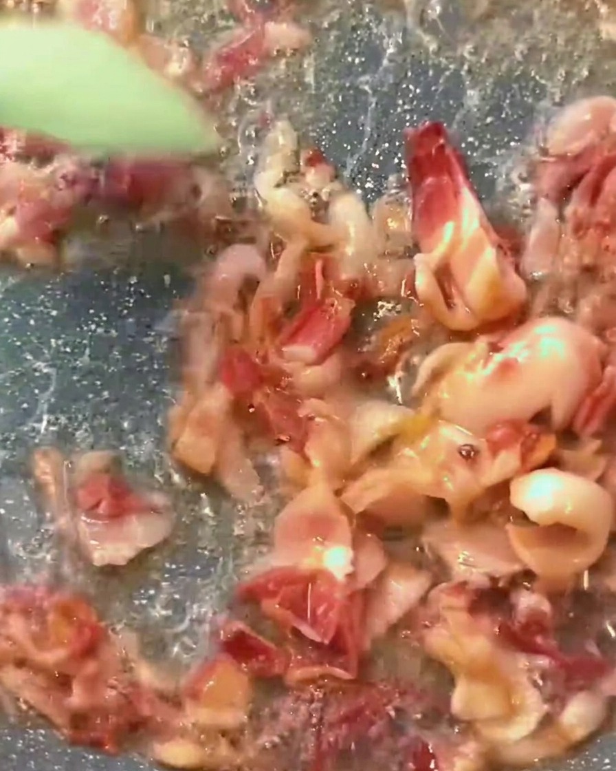 Une riche sauce tomate rouge frémissant dans une poêle, parsemée de morceaux de bacon dorés.