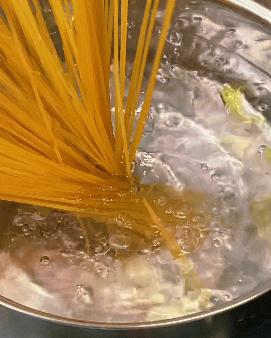 Une cuillère en bois mélangeant une sauce épaisse et savoureuse à la tomate et aux lardons dans une poêle en inox.