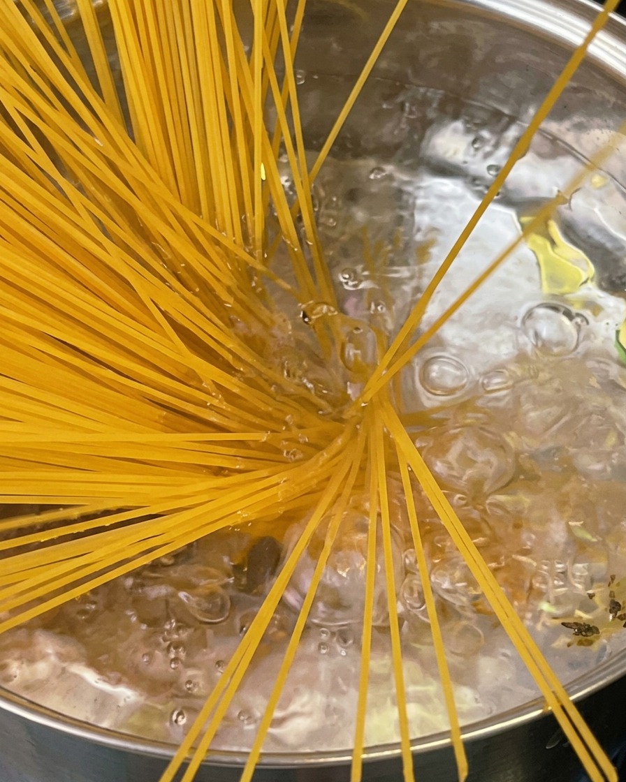 Des pâtes al dente soulevées dune marmite avec une cuillère à spaghettis, dégageant un nuage de vapeur.