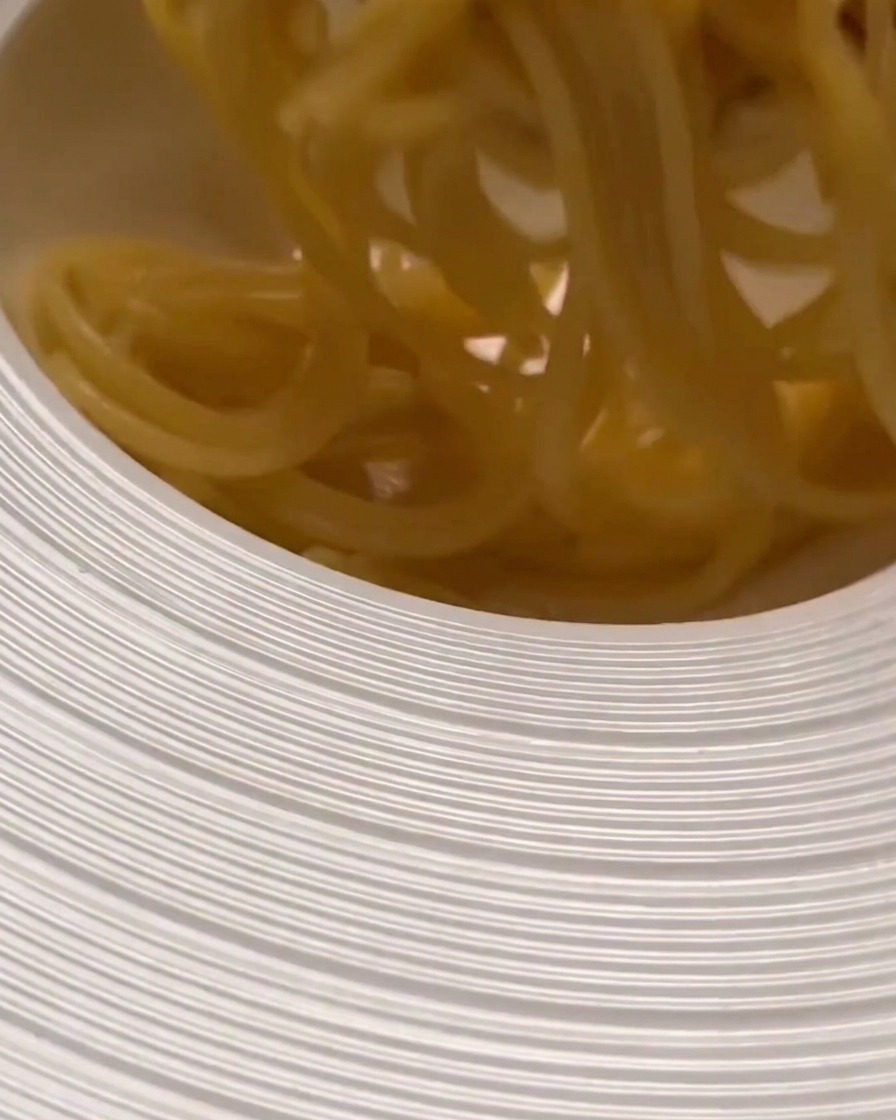 Des pâtes cuites transférées dans un grand plat de service, prêtes à être mélangées à la sauce.