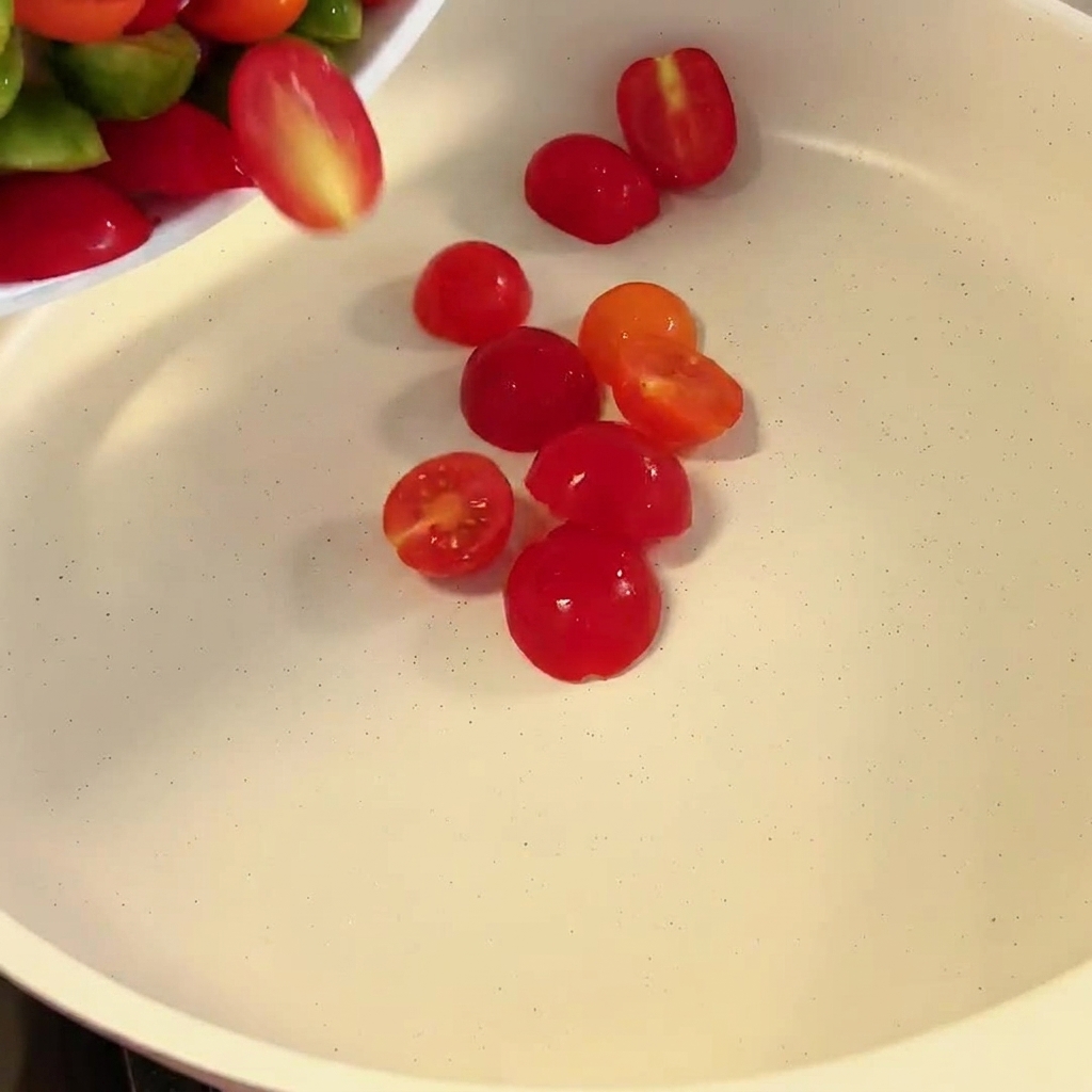 Tomates cerises coupées en deux tombant dans une poêle.