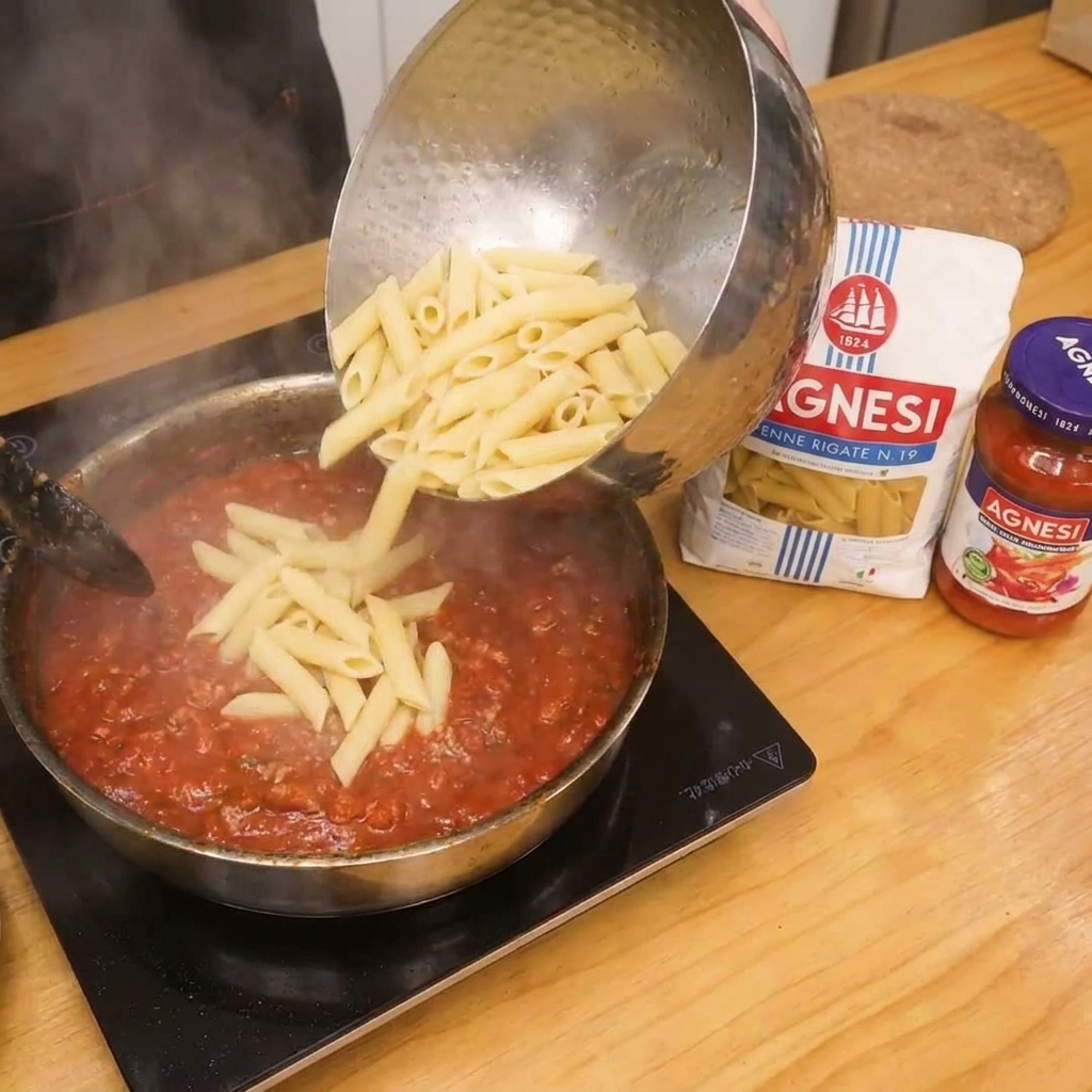 Les pennes sont ajoutées à la sauce tomate au bacon pour le mélange final.