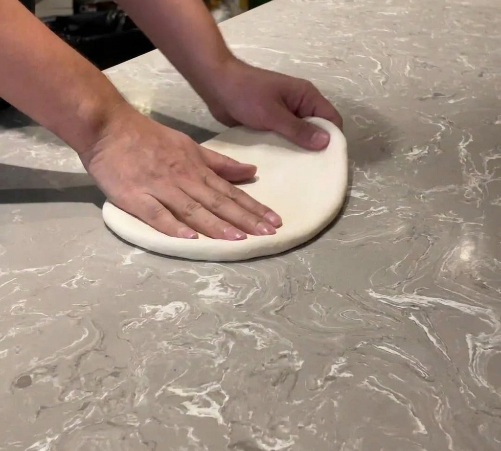 Gros plan sur des mains étalant une boule de pâte à pizza sur un plan de travail en marbre.