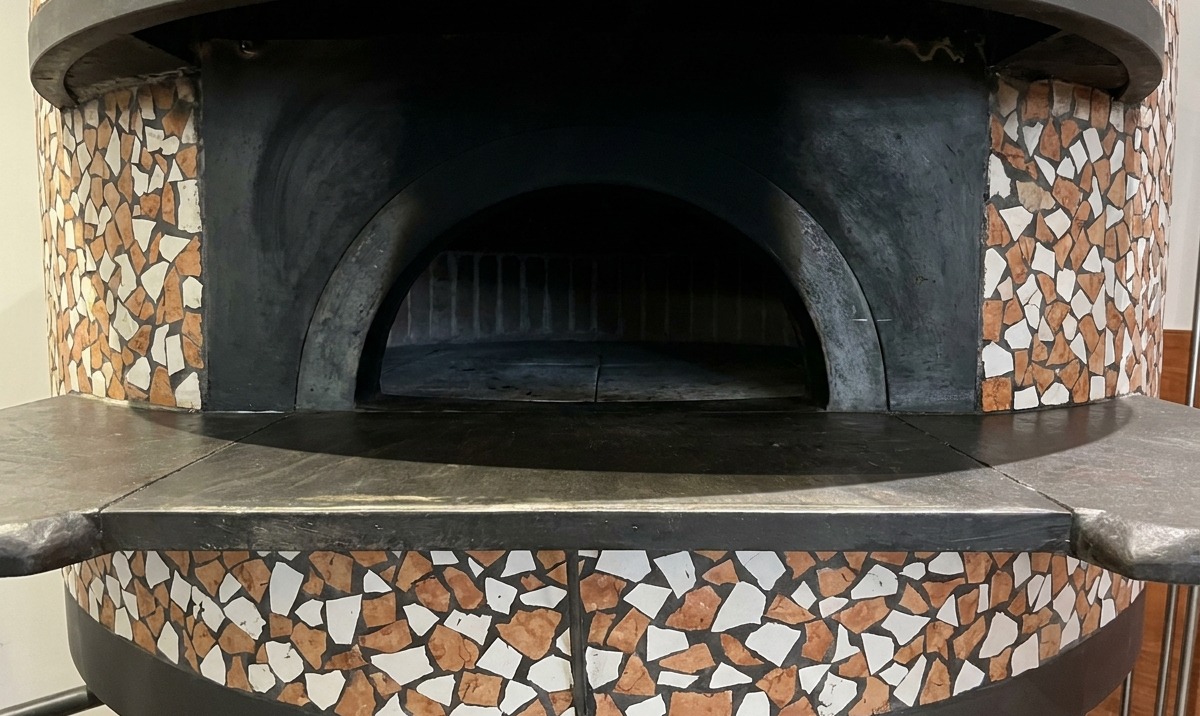 Une pizza en cours de cuisson dans un four à briques, les bords de la croûte gonflant près des flammes.