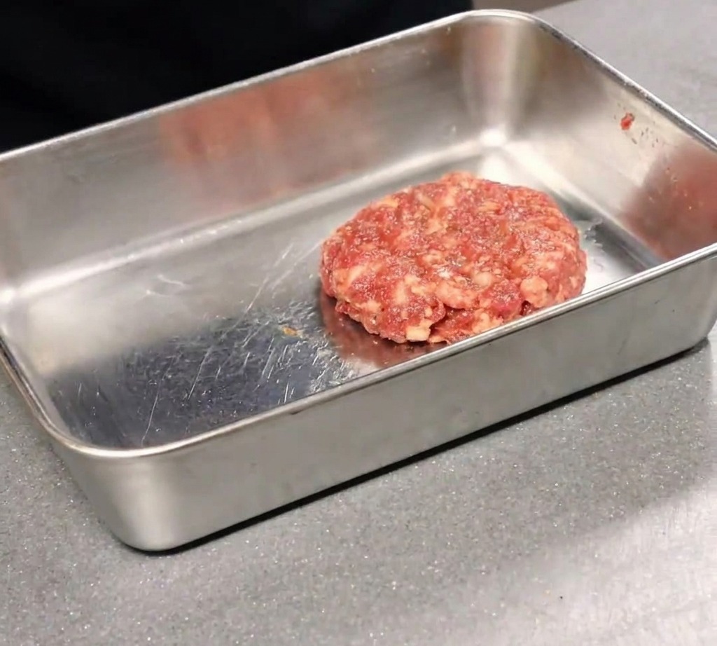 Une pizza tout juste sortie du four étant découpée en parts avec une roulette sur une planche en bois.