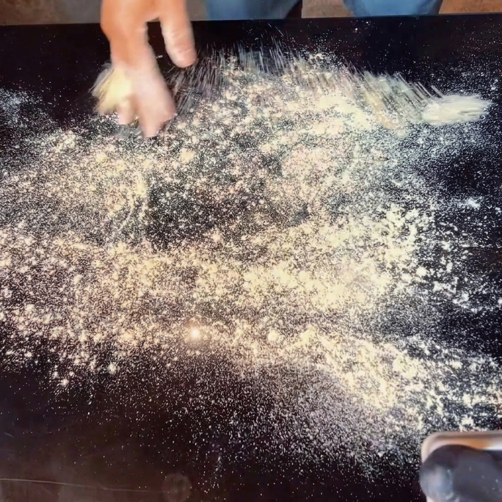 Mains étalant la pâte à pizza sur un plan de travail fariné.