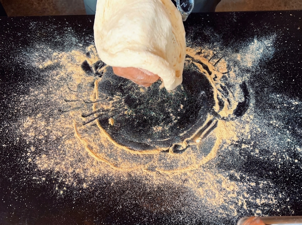 Une main étirant un morceau de pâte à pizza dans les airs au-dessus dune surface noire.