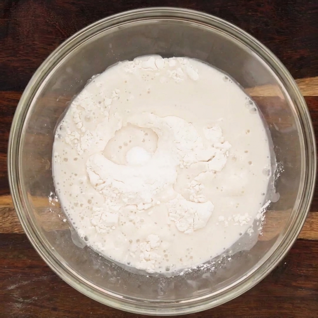 Le mélange des ingrédients secs et liquides dans un bol en verre, formant une pâte daspect encore irrégulier.