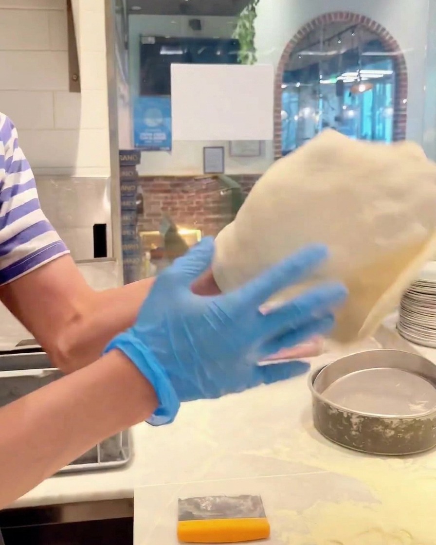 Mains faisant pivoter la pâte à pizza pour létirer en cercle.