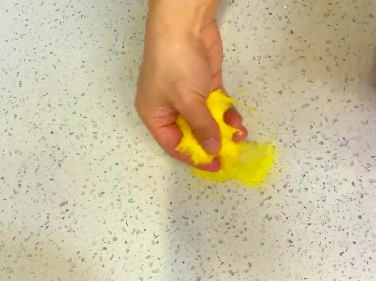Une pâte à pizza ronde étalée sur un plan de travail parsemé de semoule de maïs.