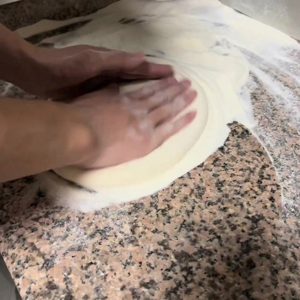 Mains pressant et étirant délicatement une pâte à pizza ronde sur un plan de travail fariné.