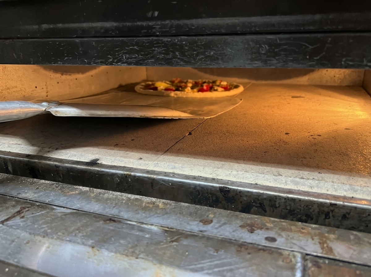 Faire glisser une pizza fraîche assemblée dune pelle en métal dans un four brûlant sur une pierre de cuisson.