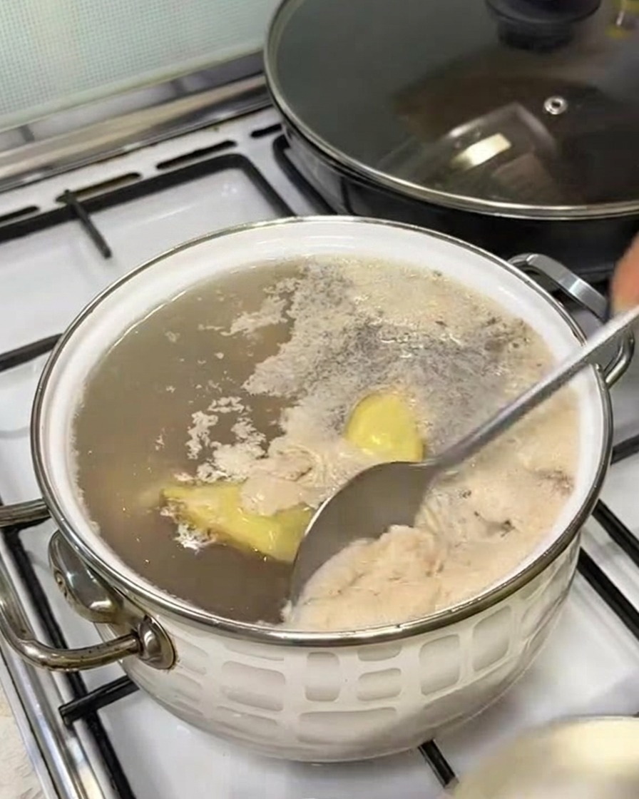 Une cuillère retirant la mousse grise à la surface de leau bouillante dans une casserole.