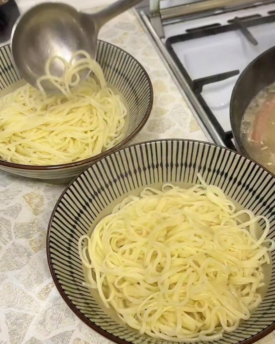 Une louche versant un bouillon de porc doré et opaque dans un bol contenant des nouilles ramen fraîchement cuites.