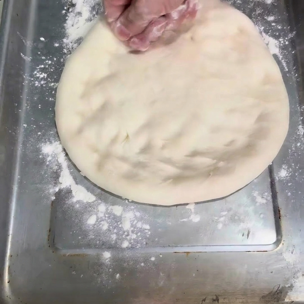 La pâte en cours daplatissement pour former un cercle sur une plaque de cuisson.