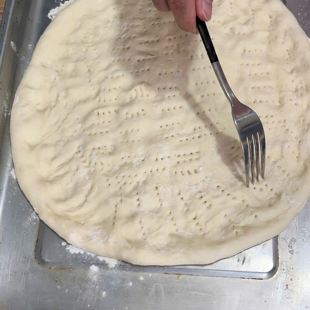 Une fourchette piquant la base de pâte aplatie sur la plaque de cuisson.
