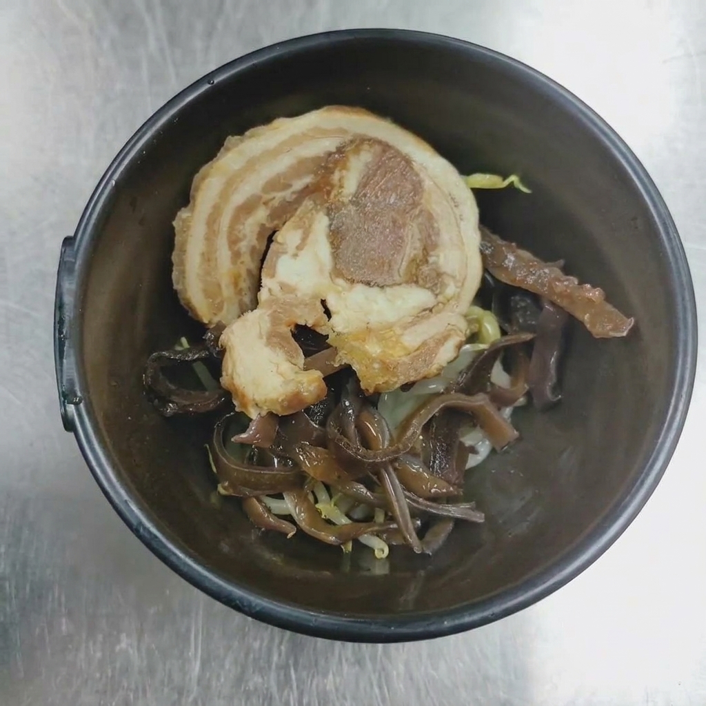 Gros plan dun bol de service contenant du porc chashu roulé et des champignons auriculaires prêts à être dressés.