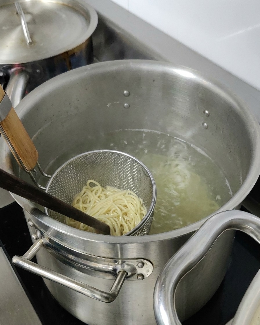 Nouilles ramen bouillant dans un panier passoire en métal immergé dans une grande casserole deau chaude.