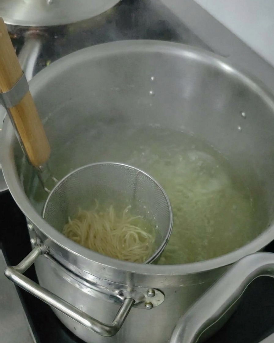 Nouilles ramen cuites soulevées dans une passoire pour égoutter lexcès deau avant dêtre ajoutées au bol.