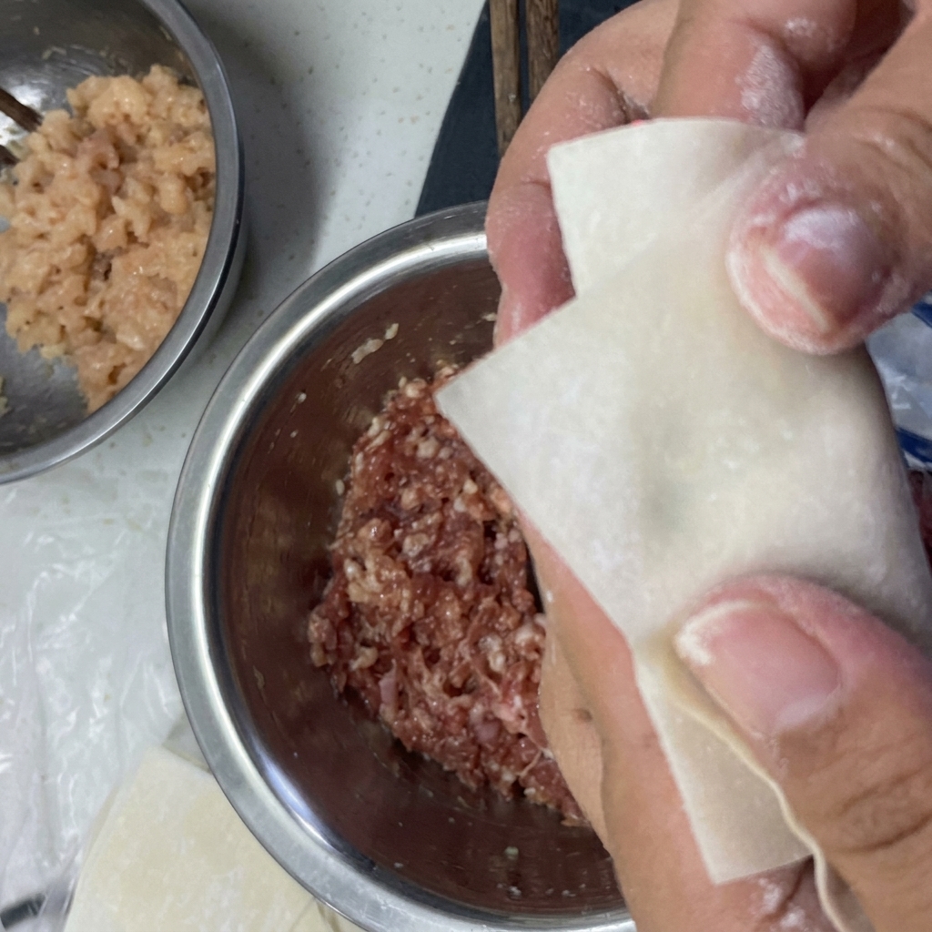 Mains pliant une feuille de wonton autour de la farce et scellant les bords avec de leau.