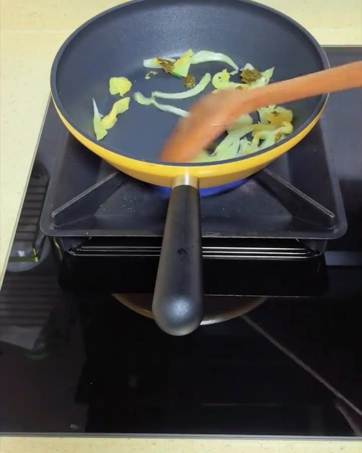 Moutarde marinée sautée dans une poêle jaune avec une spatule en bois.