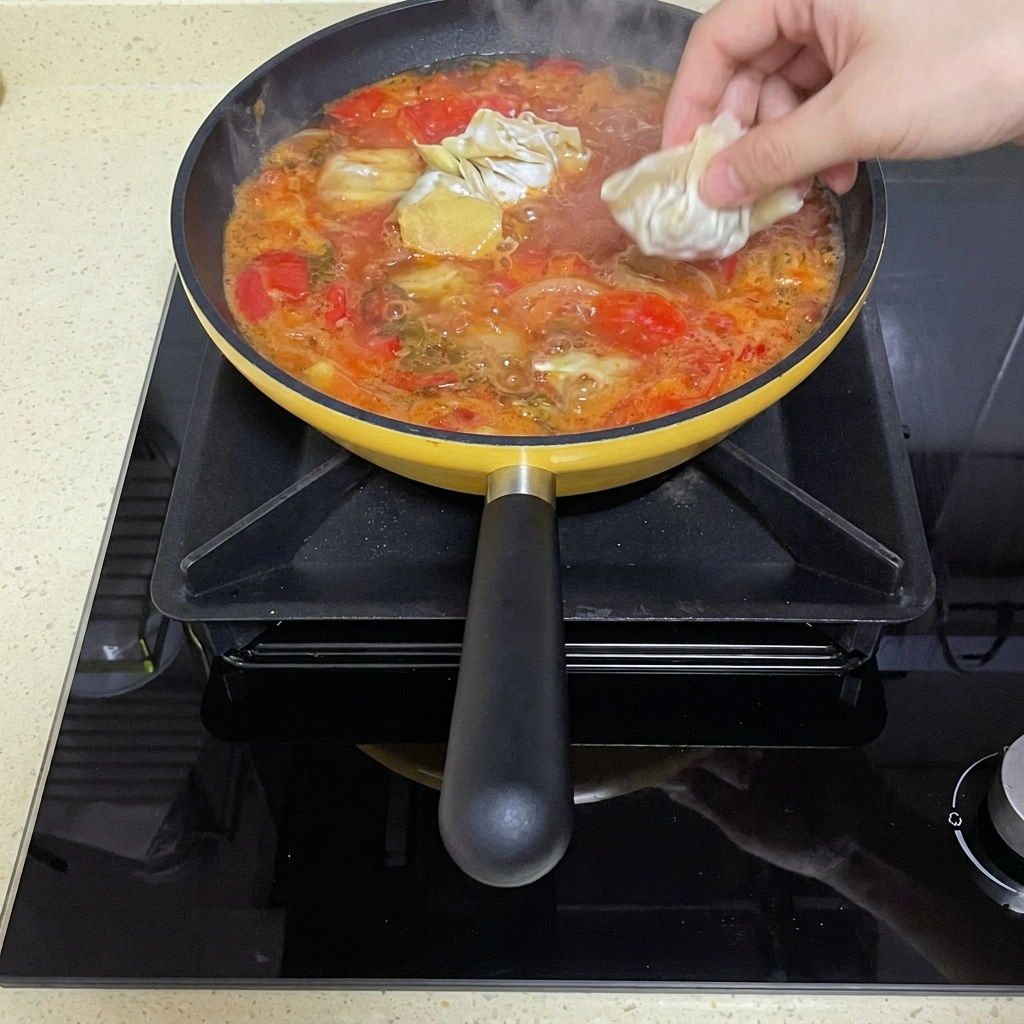 Wontons crus pliés ajoutés dans le bouillon de tomates frémissant.