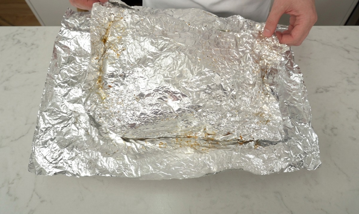 Mains ouvrant délicatement le papier aluminium pour révéler une grande pièce de côtes de bœuf rôties.