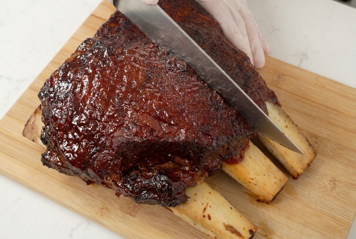 Un couteau de chef tranchant une pièce de viande caramélisée sur une planche en bois, montrant la texture juteuse.