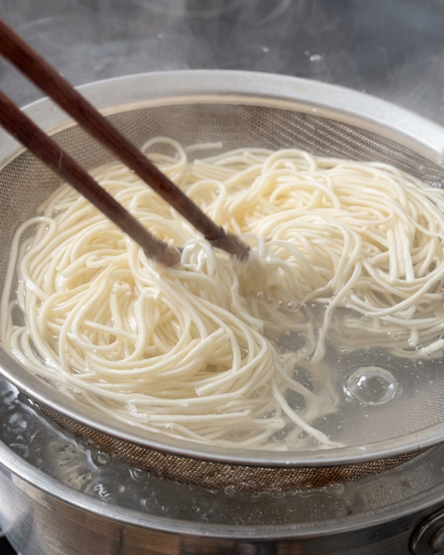 Nouilles ramen fraîches retirées de leau bouillante avec une passoire en métal à laide de baguettes en bois.