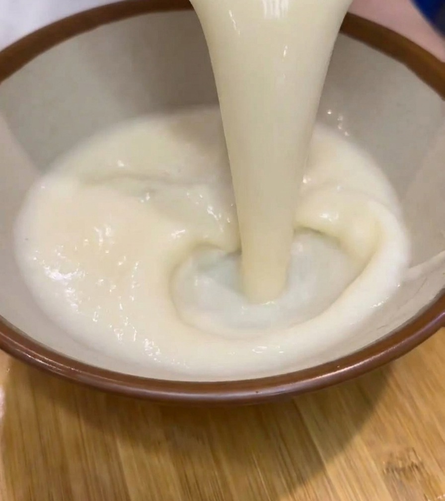 Bouillon de ramen blanc, épais et crémeux, versé depuis une carafe dans un bol en céramique à bord brun.