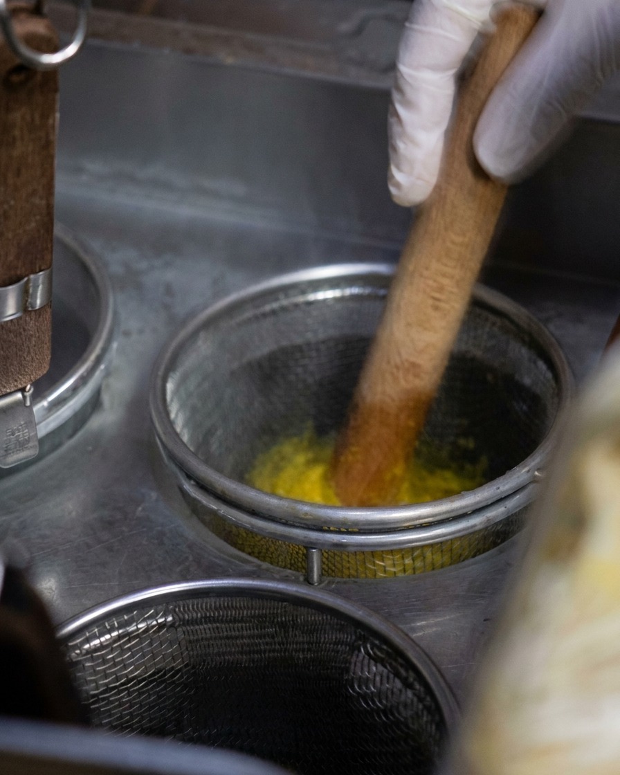 Un panier métallique rempli de nouilles jaunes remuées avec un ustensile en bois dans une casserole deau bouillante.