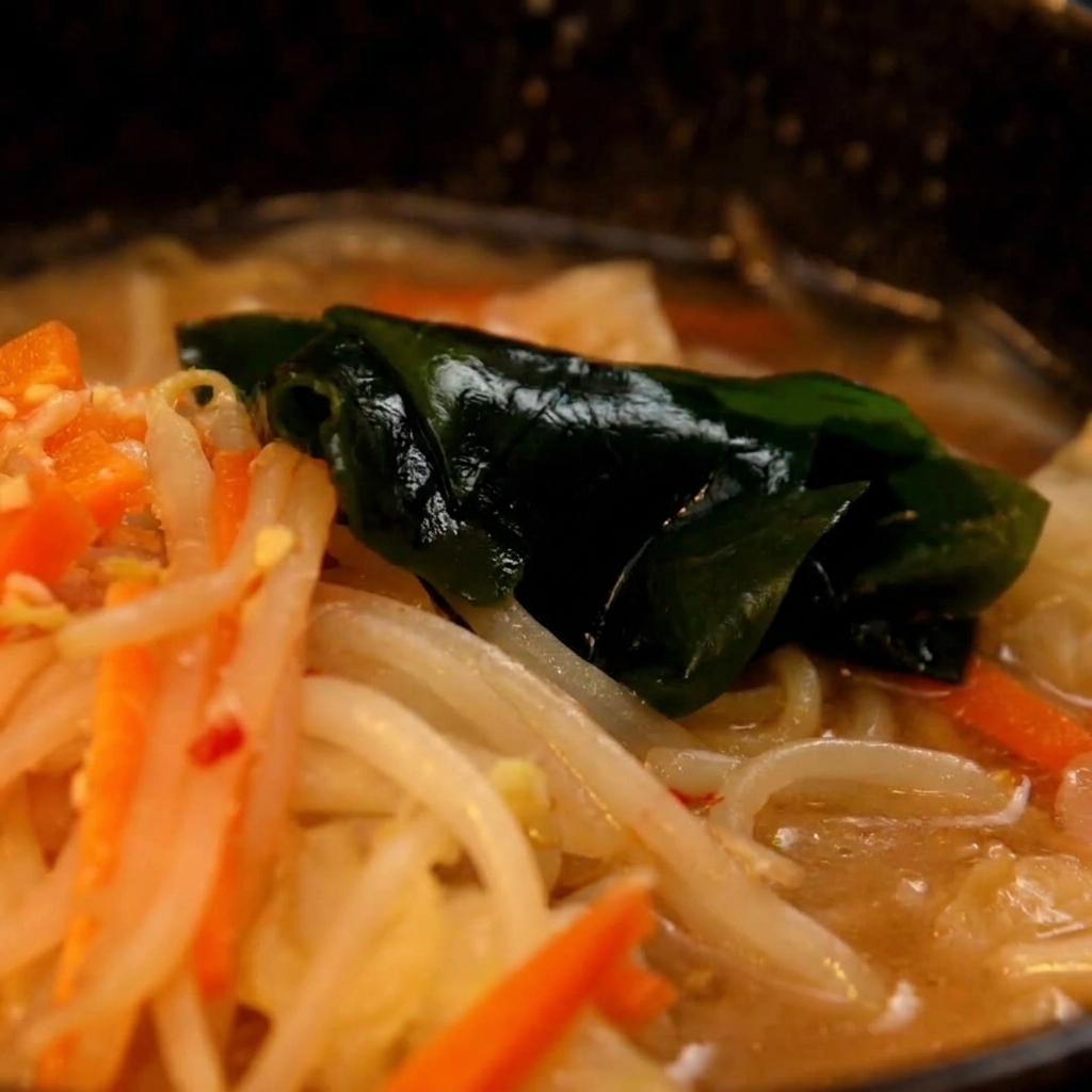 Nouilles ramen cuites transférées dune casserole vers le bol contenant la base de soupe au miso.