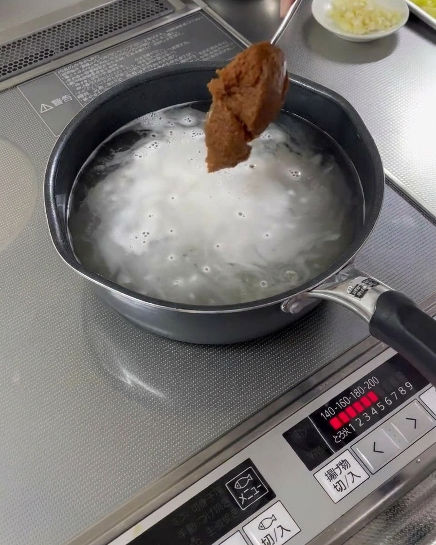 Une cuillerée de pâte miso ajoutée à une casserole de bouillon bouillant.
