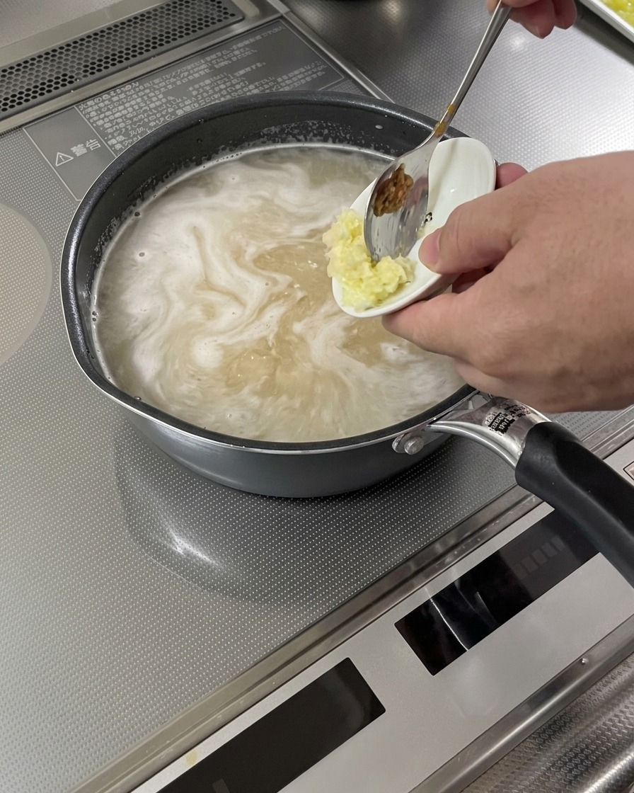 Ail et gingembre râpés ajoutés à une base de soupe frémissante.