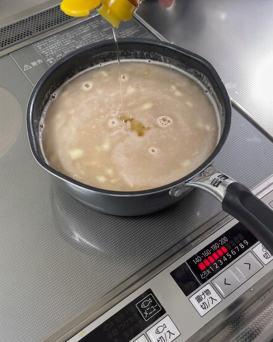 Huile de sésame versée en filet dans une base de soupe terminée.